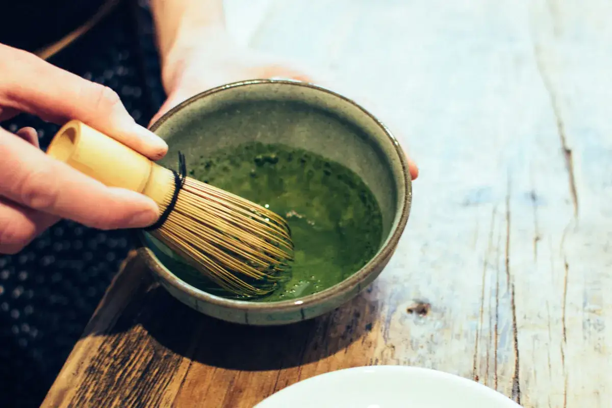 Przygotowanie zielonej herbaty matcha. Bambusowa miotełka miesza proszek z wodą w ceramicznej miseczce.