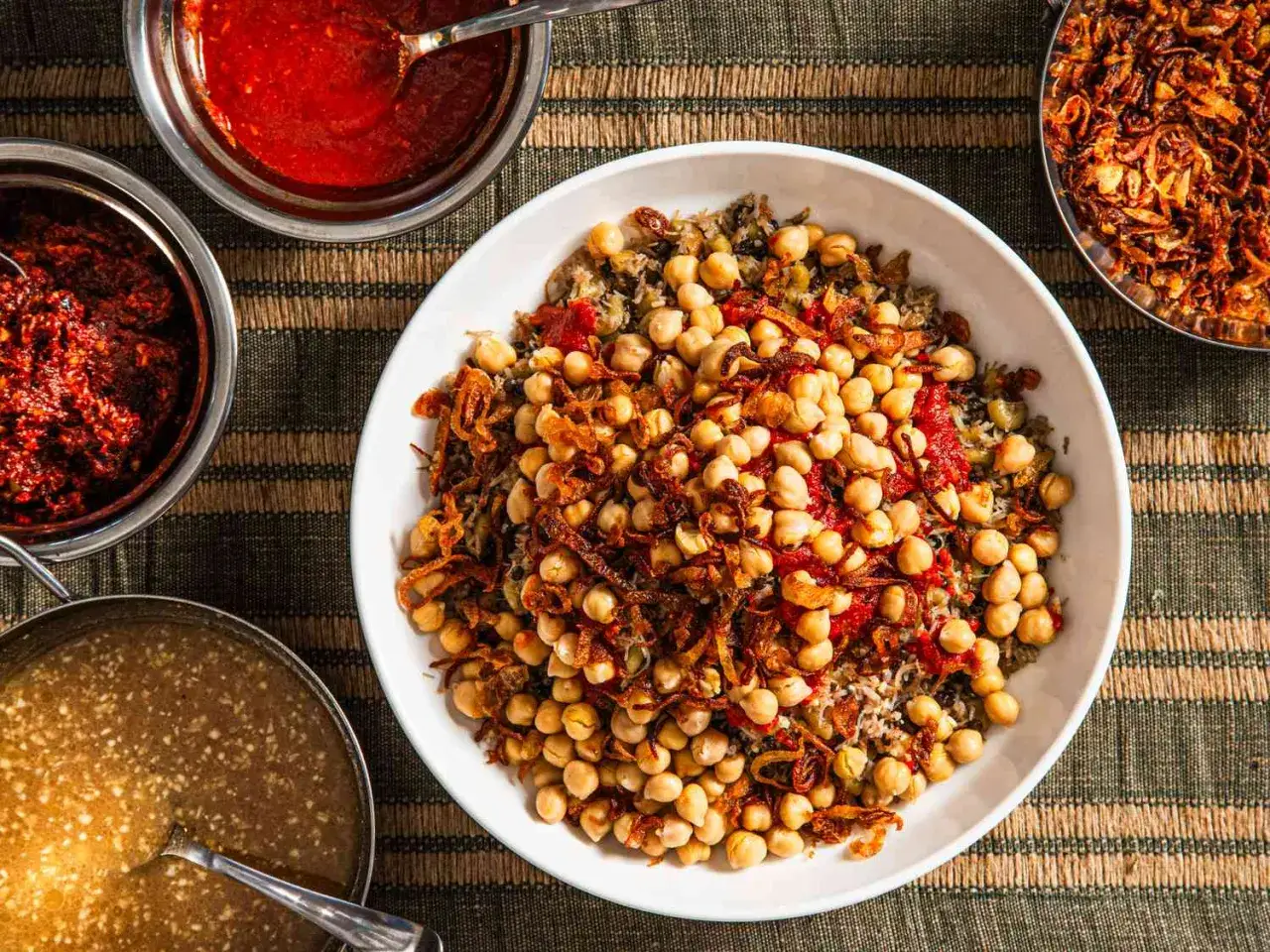 Kushari z ciecierzycą, ryżem i makaronem, polane sosem pomidorowym i posypane chrupiącą cebulką. Obok sosy i pikantny sambal. To właśnie jest sambal co to za danie!