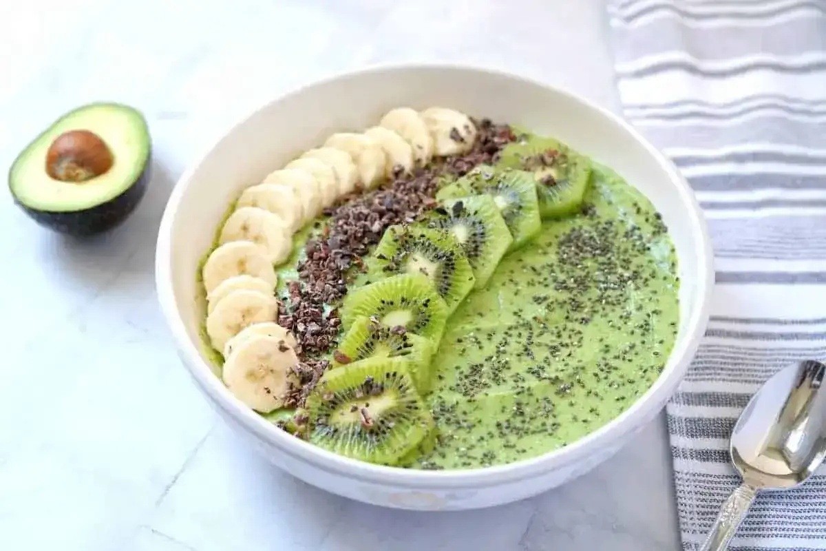 Zielony koktajl z awokado, kiwi i banana, udekorowany plasterkami banana, kiwi, kakao i nasionami chia. Pyszne i zdrowe śniadanie.