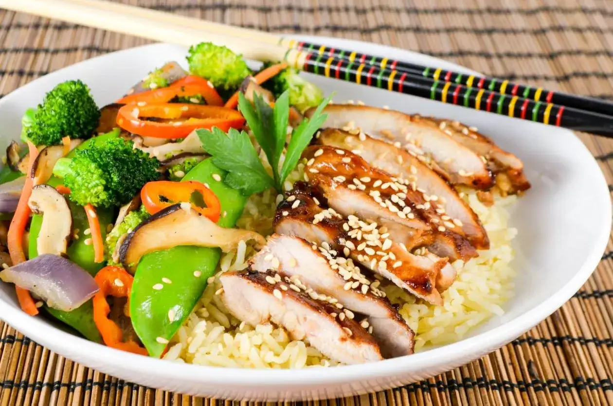 Pyszny kurczak z gotowym sosem teriyaki, podany z ryżem i kolorowymi warzywami. Posypany sezamem.
