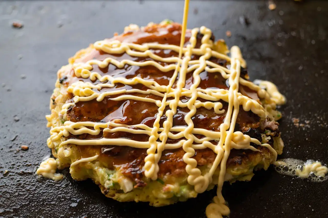 Okonomiyaki polane sosem i majonezem japońskim na gorącej płycie.
