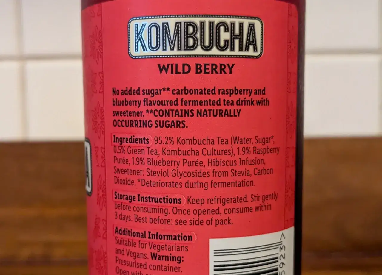 Etykieta kombuchy Wild Berry. Informacje o składnikach i ostrzeżenie o naturalnie występujących cukrach, co może sugerować potencjalną szkodliwość dla niektórych osób.