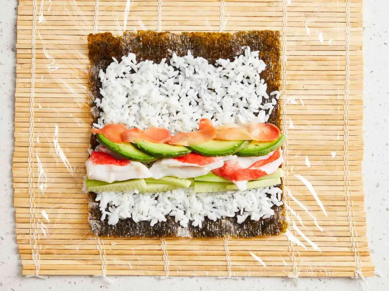Jak zrobić sushi: na nori ryż, paluszki krabowe, ogórek, awokado i łosoś. Rolowanie na macie bambusowej.