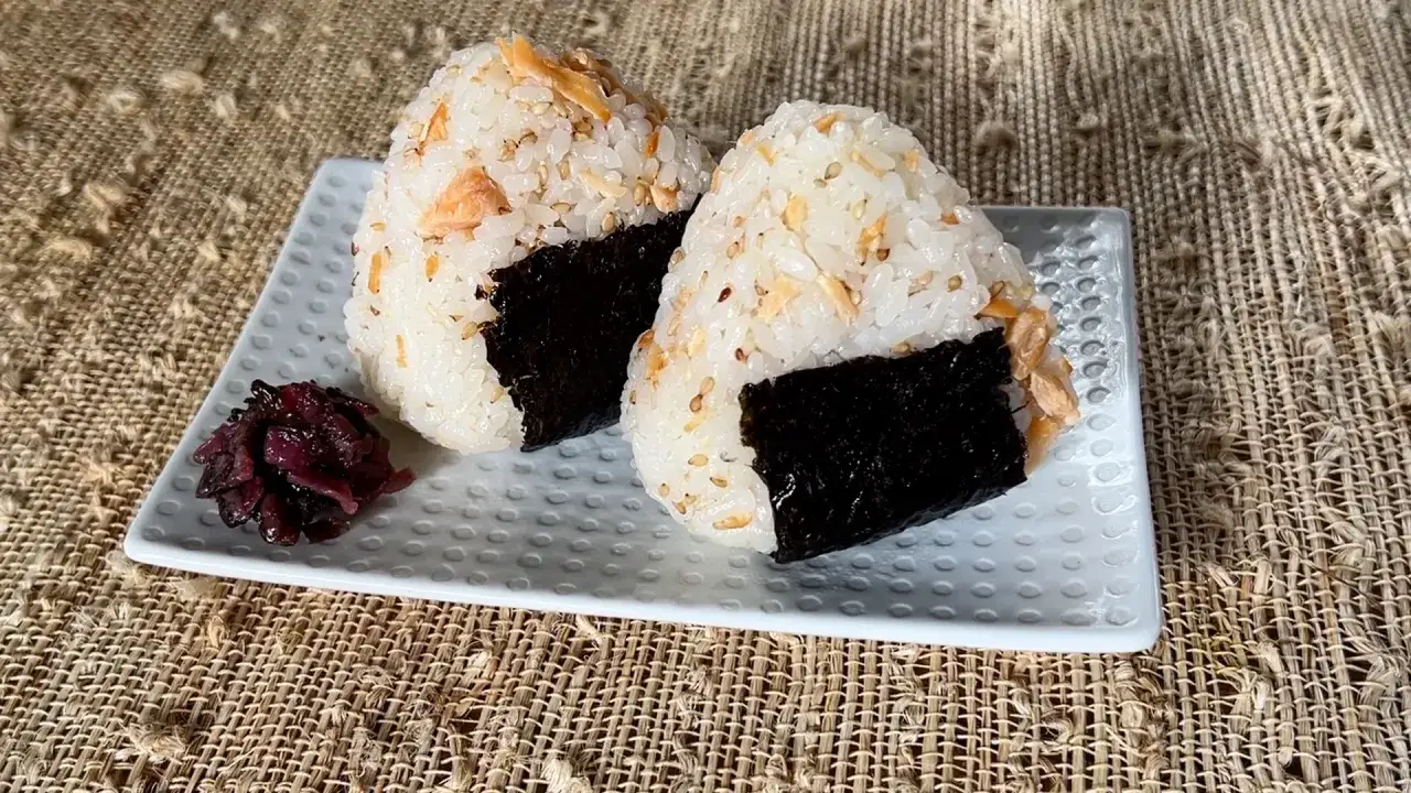 Dwa pyszne onigiri z łososiem, owinięte w nori, podane z marynowaną rzodkiewką.