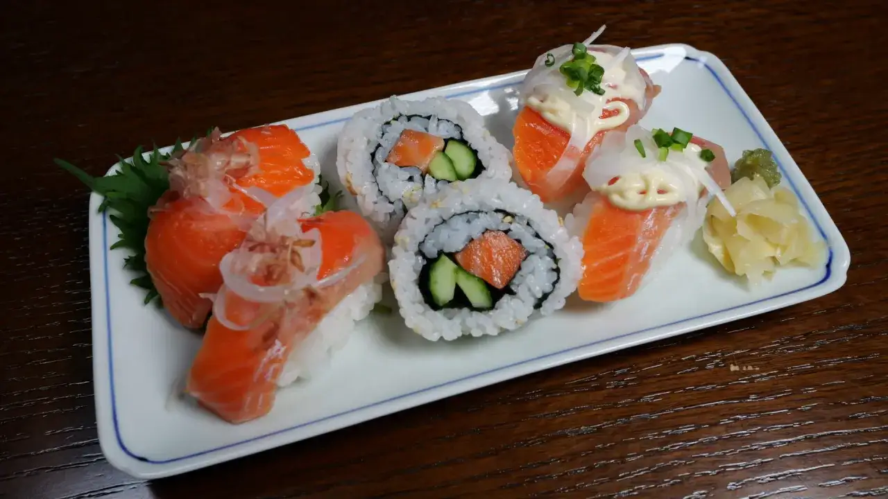 Pyszny surowy łosoś do sushi, podany na talerzu z ryżem, ogórkiem i dodatkami.