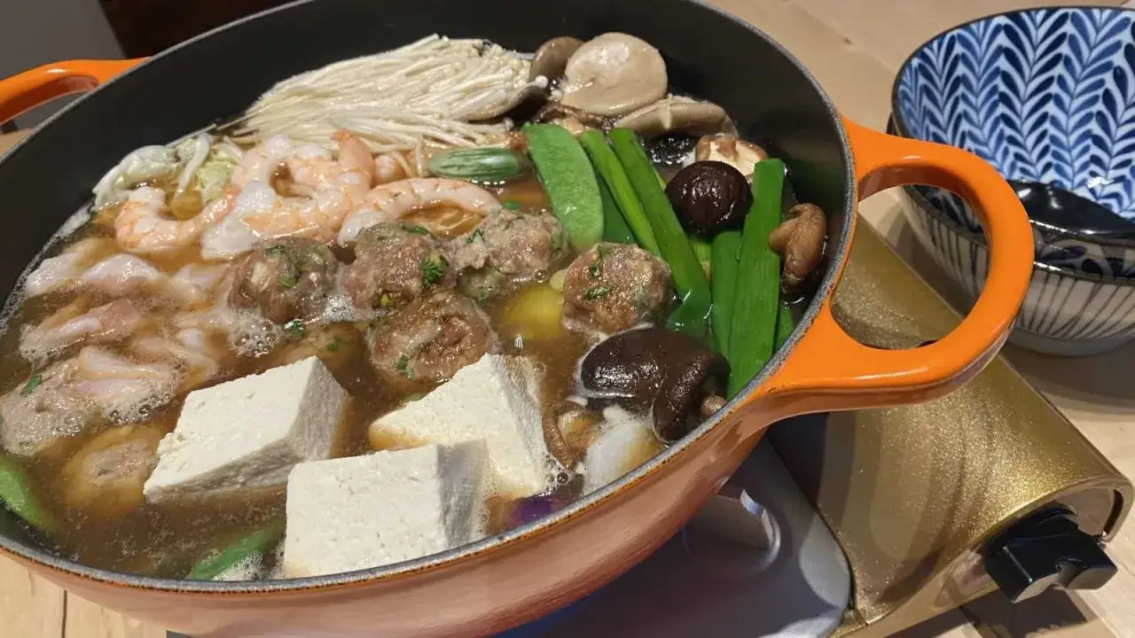Gorący garnek z sosem sukiyaki, pełen krewetek, klopsików, tofu, grzybów i makaronu.
