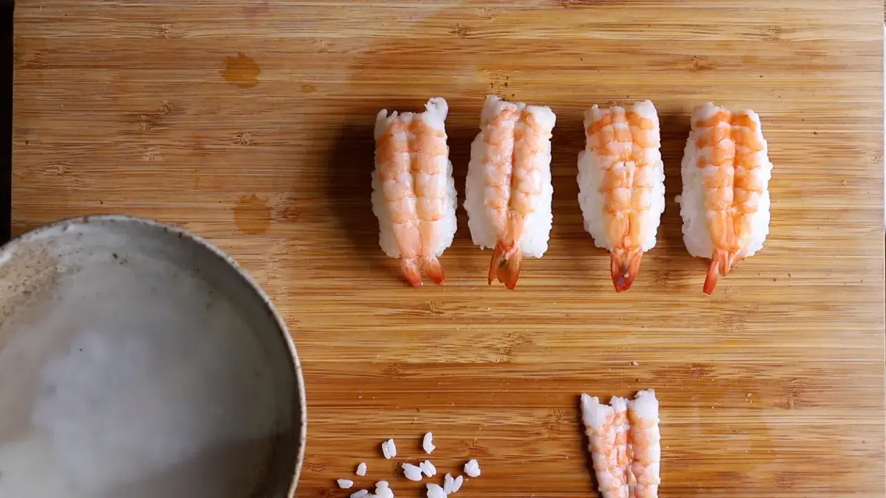 Cztery gotowe nigiri z krewetkami do sushi i jedna krewetka obok.