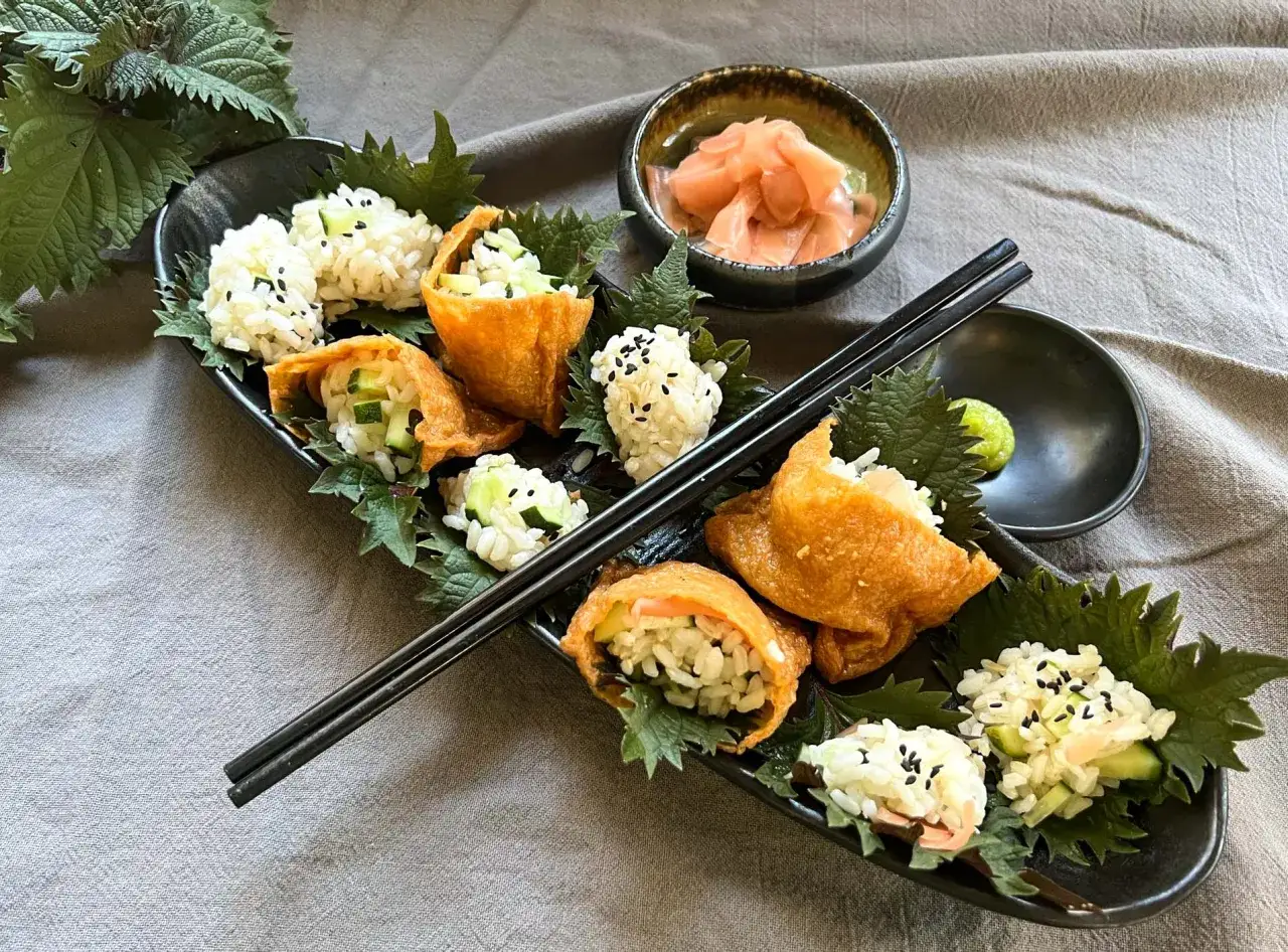 Inari sushi z ryżem i ogórkiem, podane na liściach shiso. Obok miseczka z marynowanym imbirem i wasabi. Idealne liście do sushi na przekąskę.