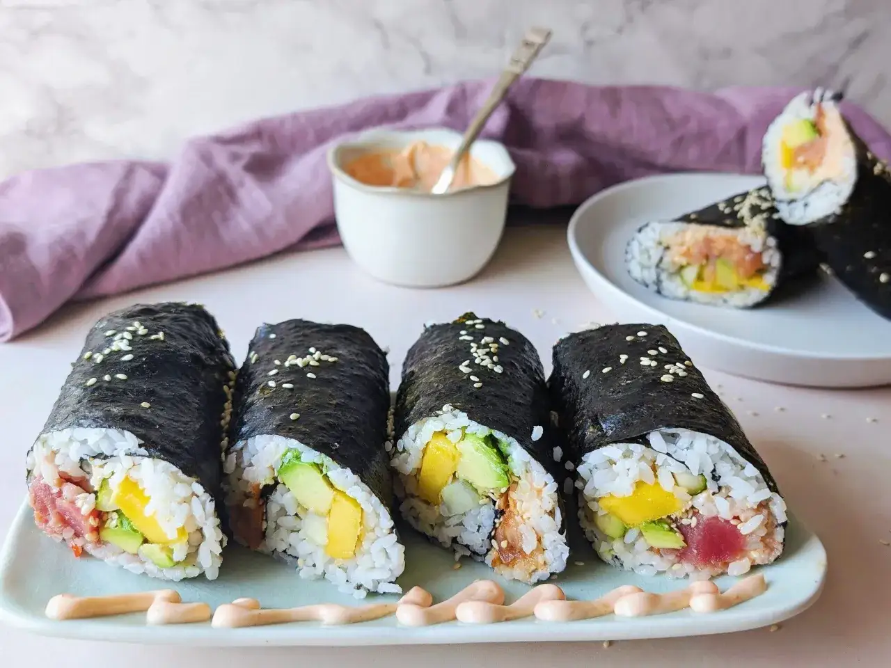 Cztery rolki sushi z awokado, mango i tuńczykiem, posypane sezamem, idealne do zawijania sushi.