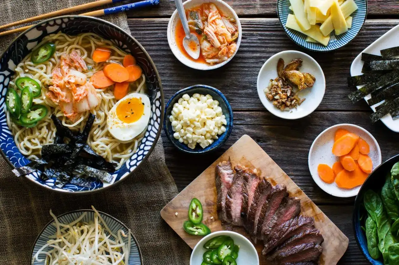 Jak zrobić ramen? Miska pełna makaronu z jajkiem, kimchi, marchewką i nori. Obok składniki: wołowina, kukurydza, kiełki, jalapeno.