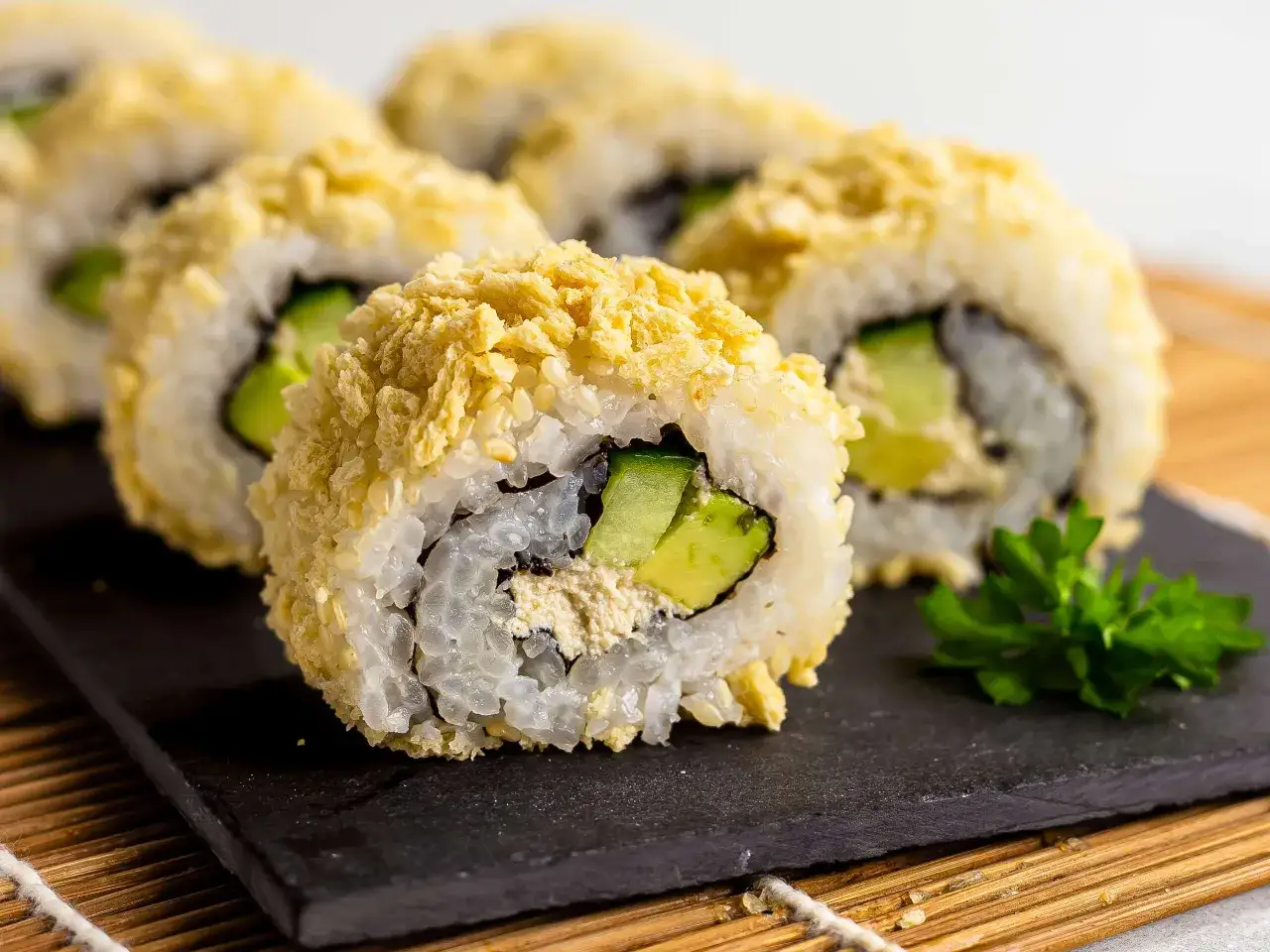 Chrupiące sushi w panierce z sezamem i awokado, podane na czarnej desce.