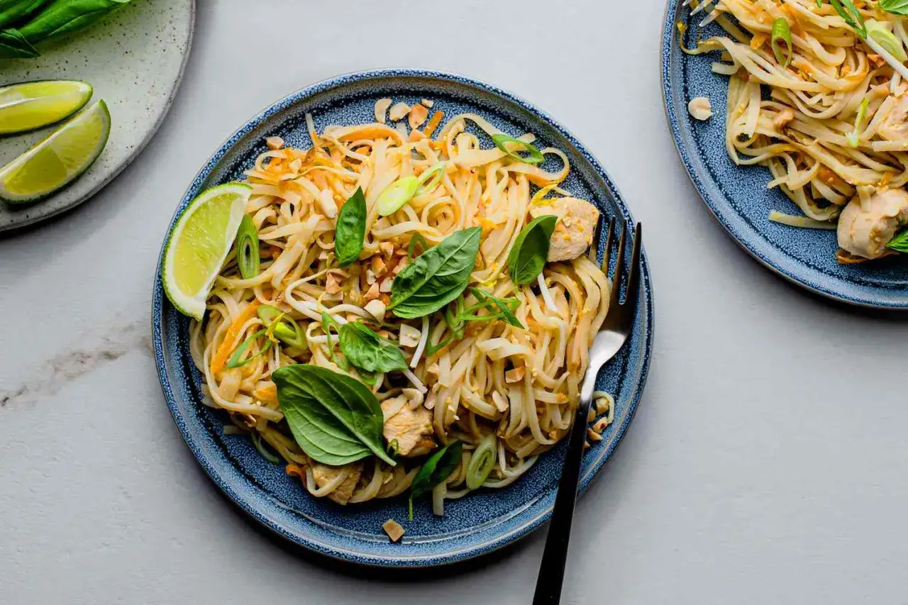 Pyszny sos pad thai z kurczakiem, makaronem ryżowym, orzeszkami ziemnymi i świeżą bazylią. Podany z ćwiartkami limonki.