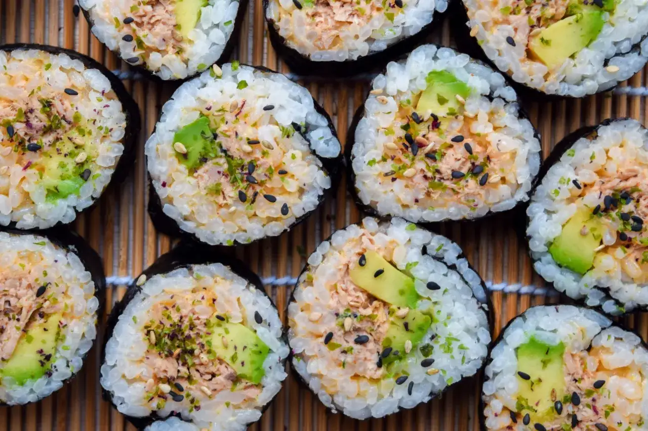 Pyszne sushi z tuńczykiem i awokado, posypane sezamem i ziołami, ułożone na bambusowej macie.