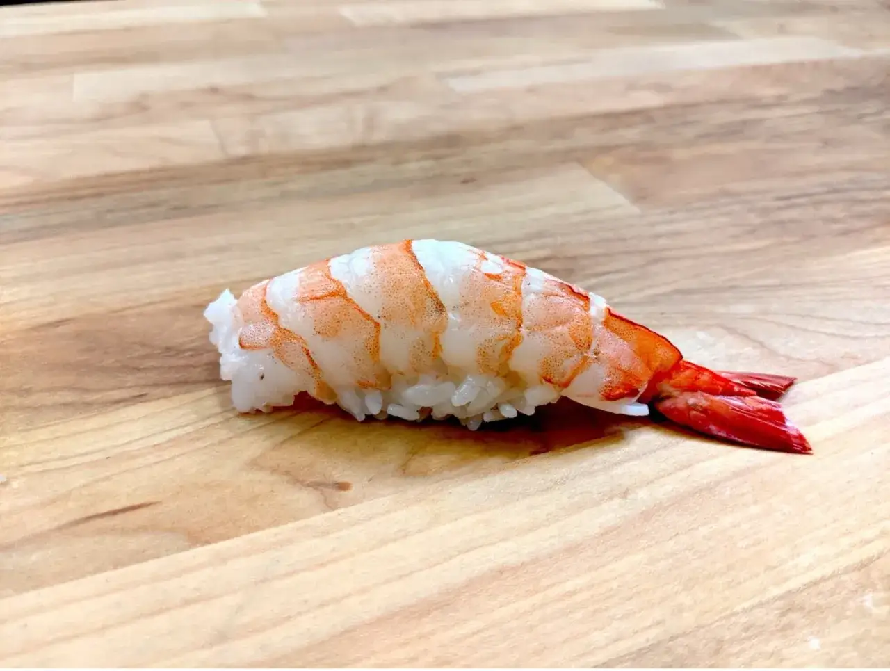 Nigiri krewetka, z soczystym, pomarańczowym mięsem na ryżu, prezentuje się apetycznie na drewnianym blacie.