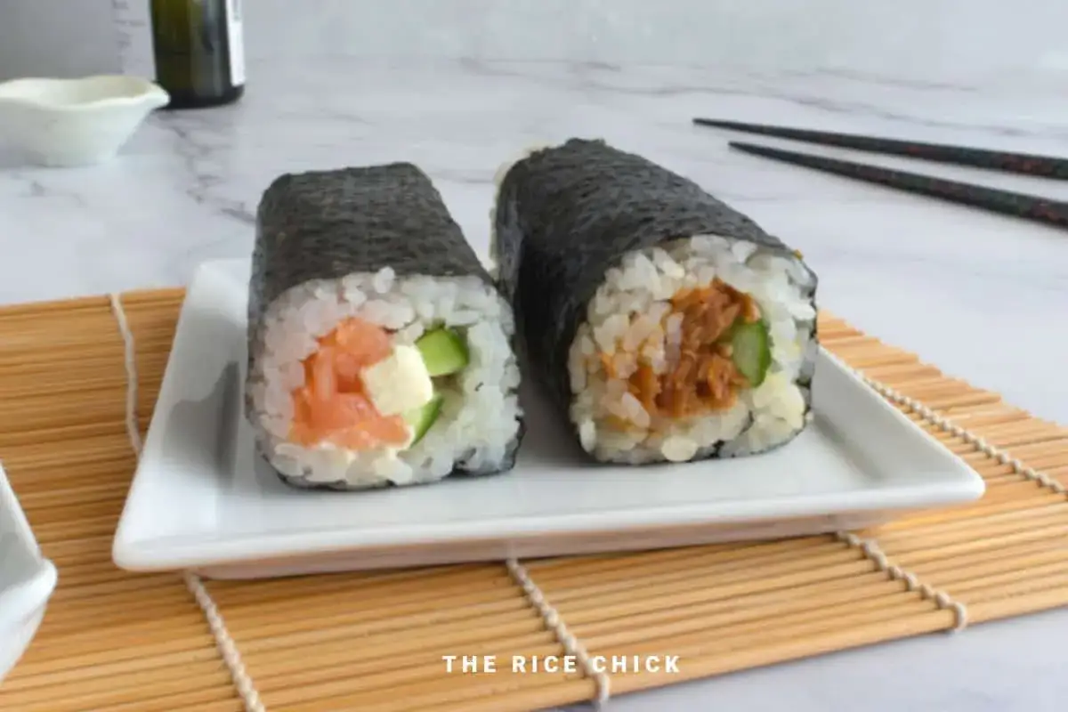Dwa sushi: futomaki z łososiem i ogórkiem oraz hosomaki z tuńczykiem i ogórkiem, na białym talerzyku.