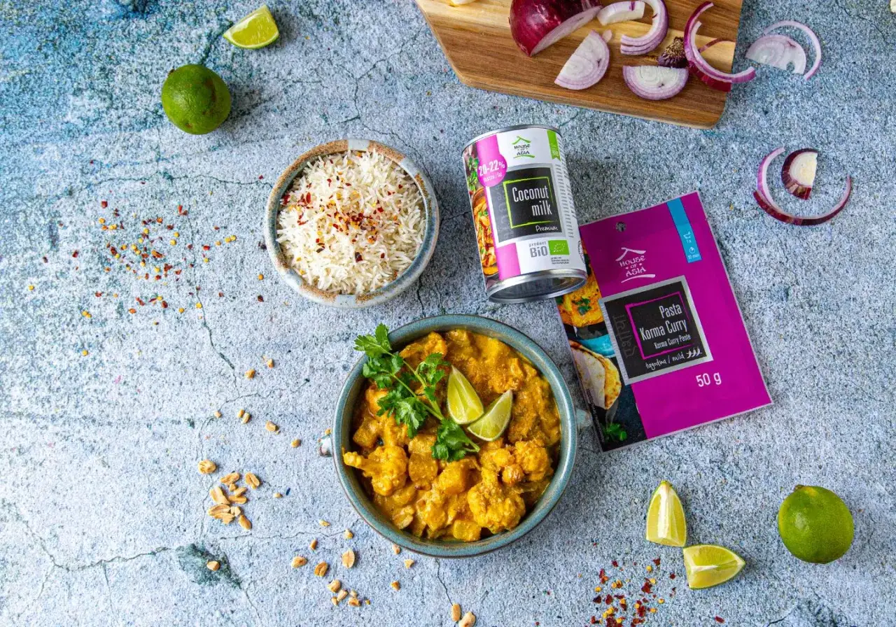 Aksamitne korma curry z kawałkami warzyw, podane z ryżem basmati. Obok puszka mleka kokosowego i opakowanie pasty korma curry.