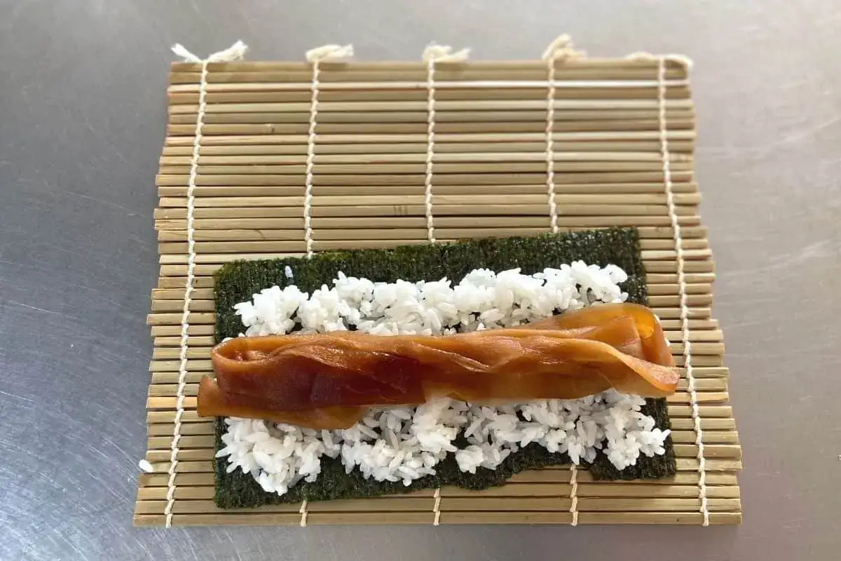 Na macie bambusowej do sushi rozłożono nori, ryż i brązowy, kandyzowany korzeń, czyli kanpyo.