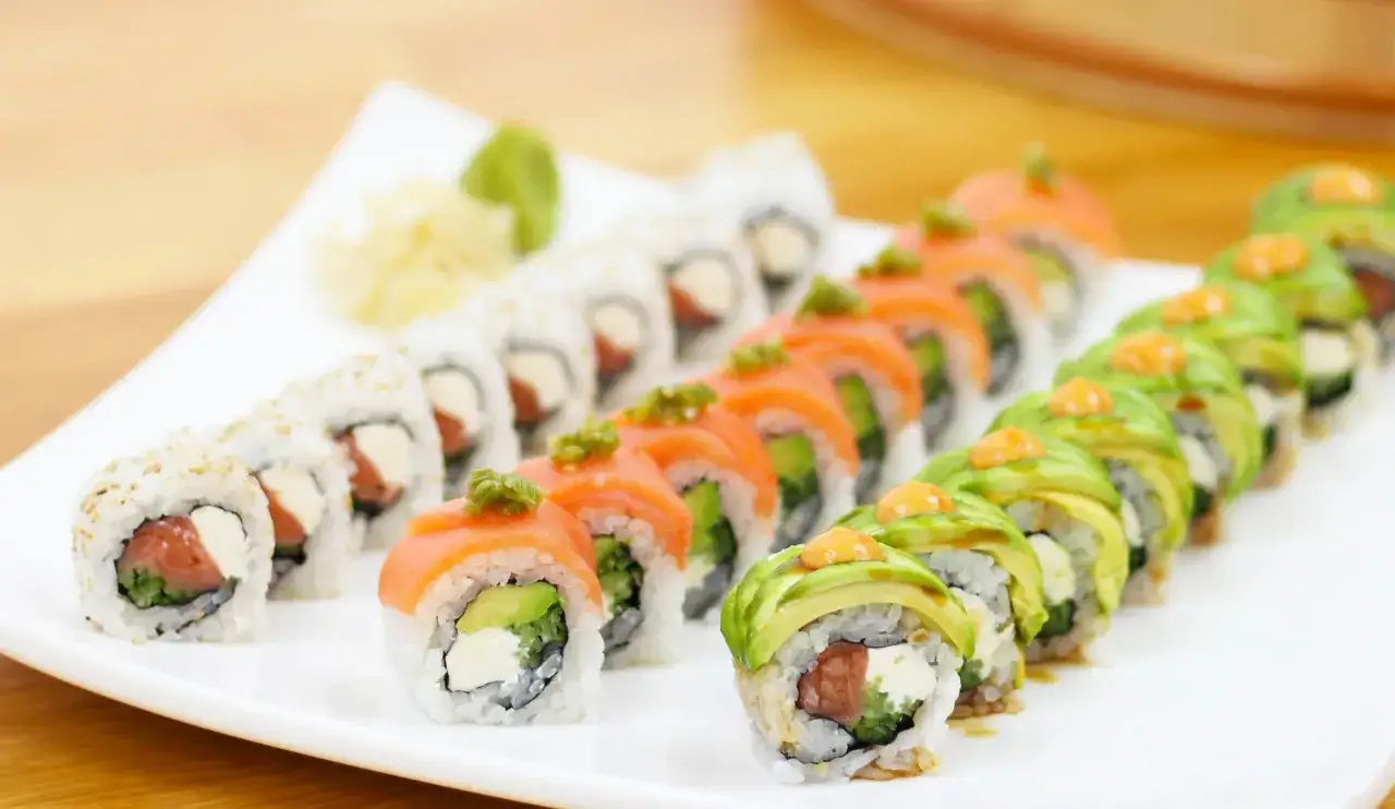 Różnorodne rolki sushi, w tym klasyczne sushi philadelphia z łososiem i kremowym serkiem, ułożone na białym talerzu.
