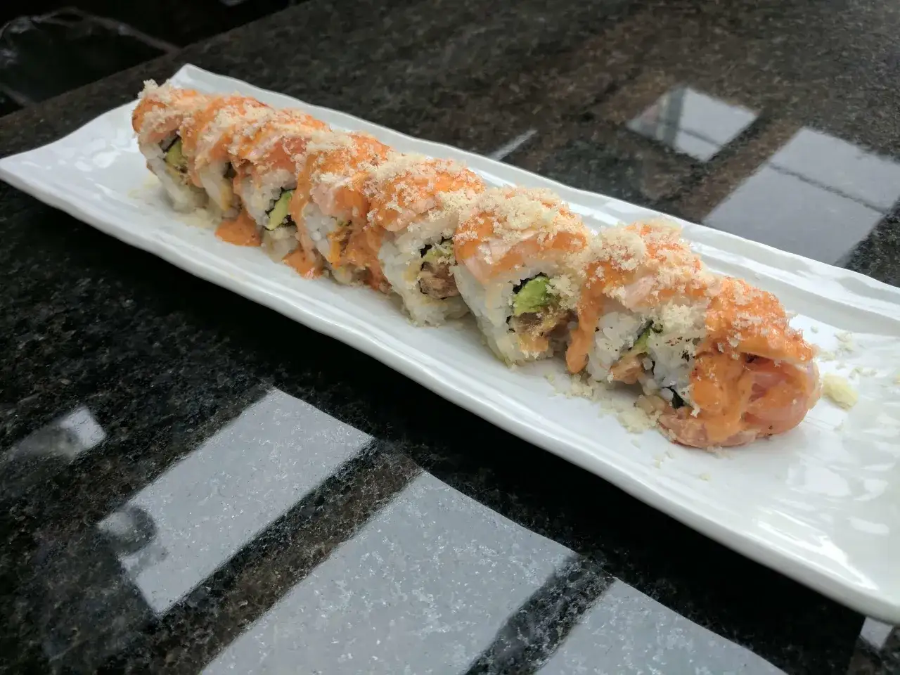Długi rolka sushi z łososiem w tempurze, polana kremowym sosem i posypana chrupiącą panierką.