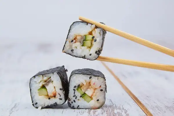 Rolka sushi z ogórkiem i rybą, podniesiona pałeczkami. Zastanawiasz się, ile octu ryżowego na 500g ryżu?