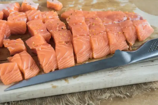 Pokrojony w kostkę i plastry łosoś, idealny do sushi, leży na desce obok noża.