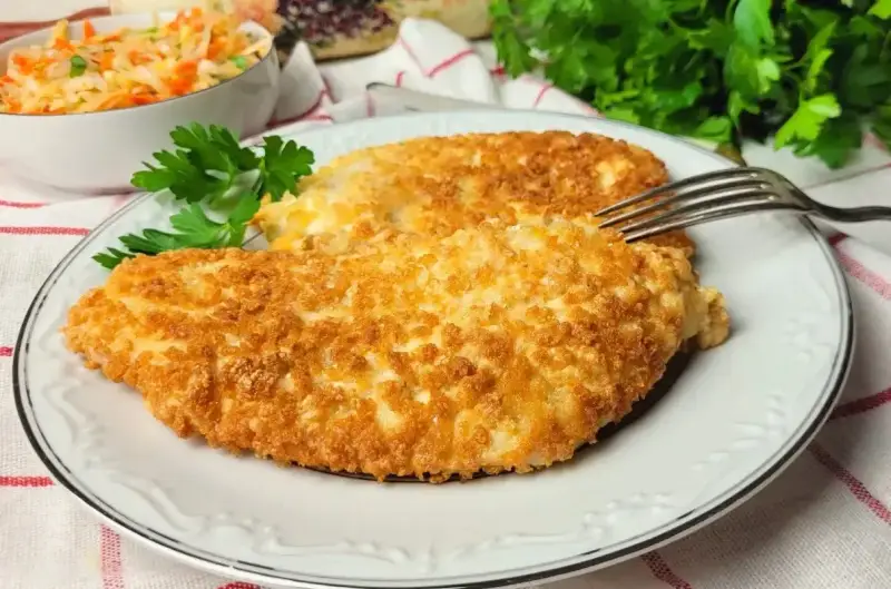 Dwa chrupiące kotlety z kurczaka w panko, podane na talerzu z sałatką z kapusty i marchewki.