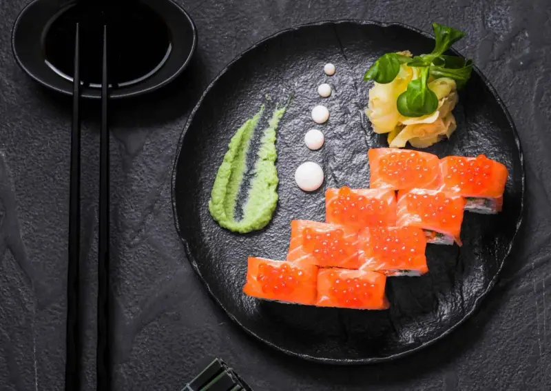 Roladki sushi z łososiem i ikrą, podane z zielonym, pikantnym wasabi prawdziwe, imbirem i sosem sojowym.